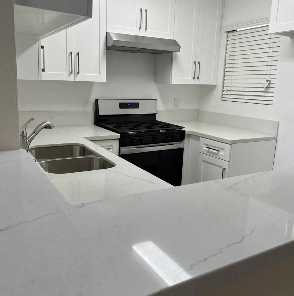 A kitchen with a stove, sink, and cabinets.