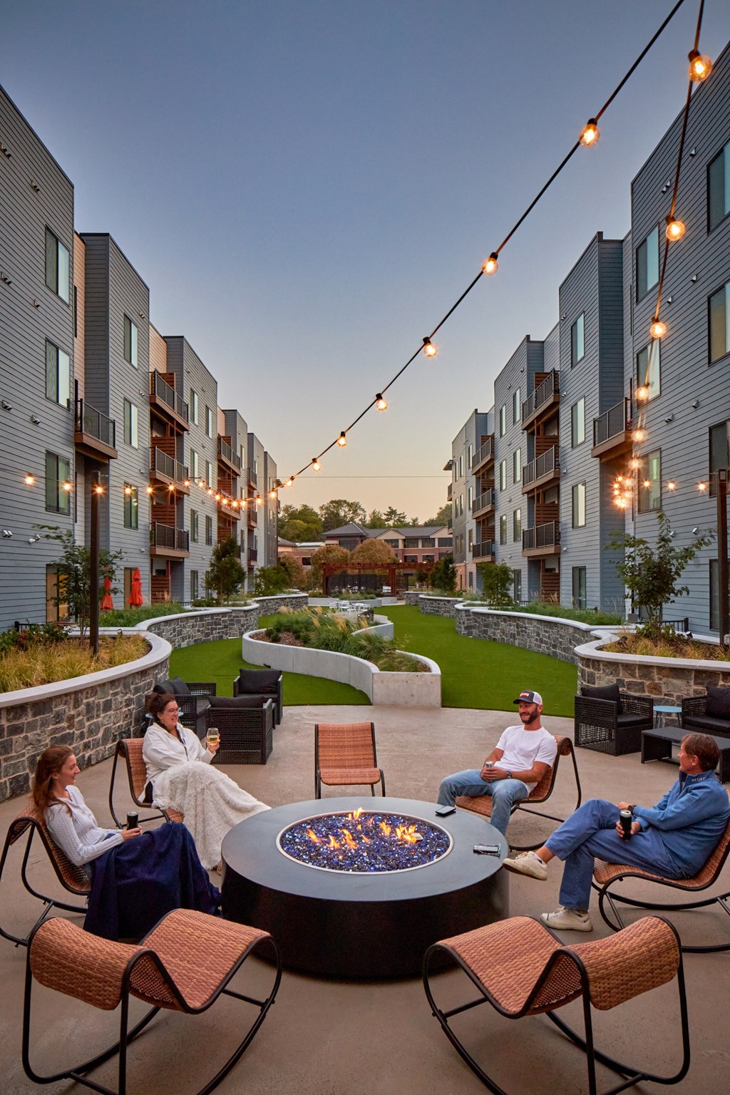 A group of people are sitting around a fire pit in a courtyard surrounded by buildings.