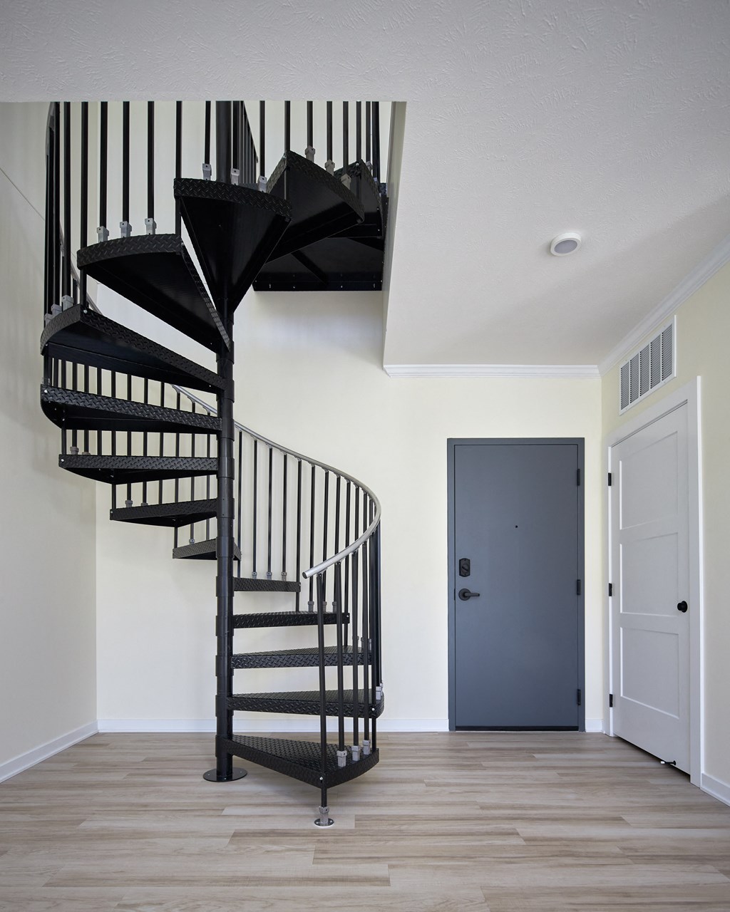 a spiral staircase in a home with white walls and a blue door