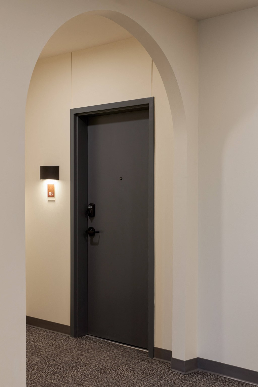 an arched hallway with a black door and a wall mounted light