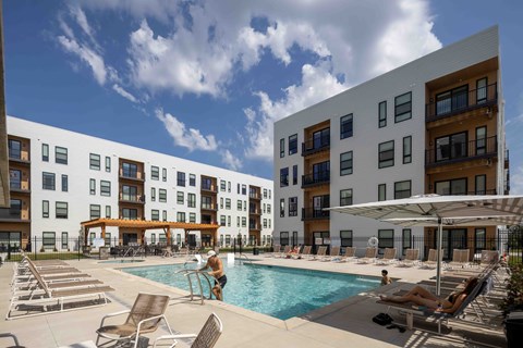 A swimming pool area with sun loungers and a person in the pool.