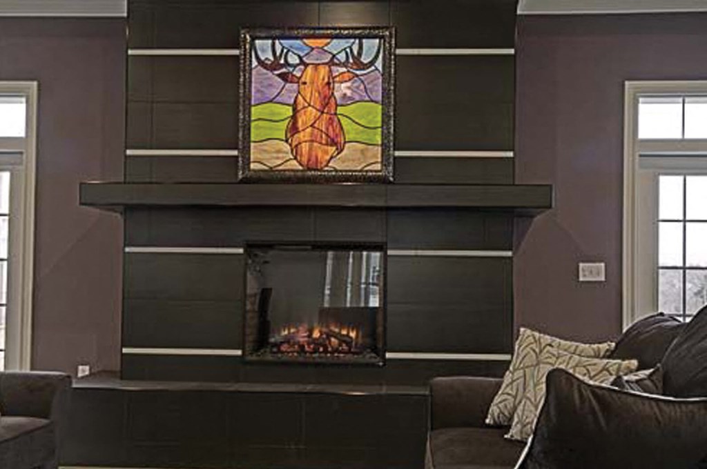 A stained glass picture of a cow is hanging above a fireplace in a living room.