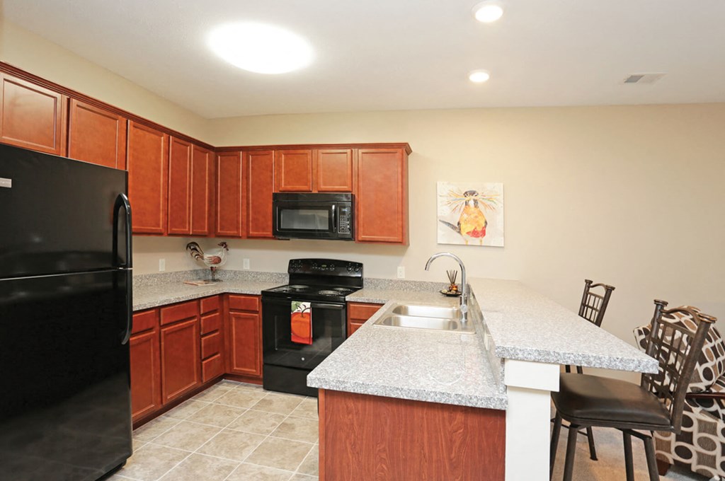 A kitchen with brown cabinets and a black refrigerator.