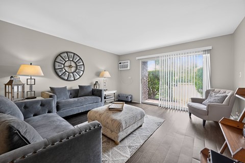 A living room with grey couches and a large clock on the wall.