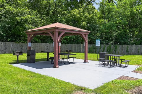 A gazebo with picnic tables is surrounded by a fence and trees.