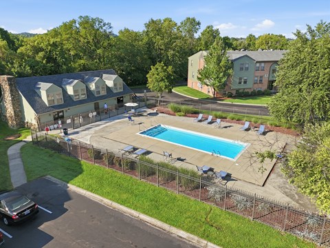 A pool surrounded by a fence and chairs with a building in the background.