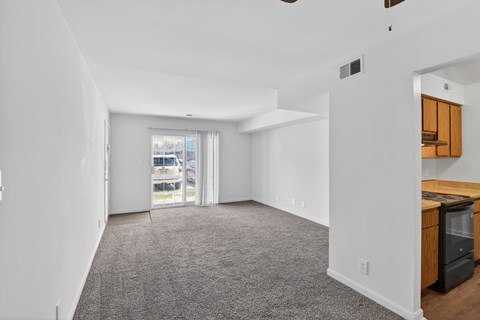 A spacious living room with a grey carpet and white walls.