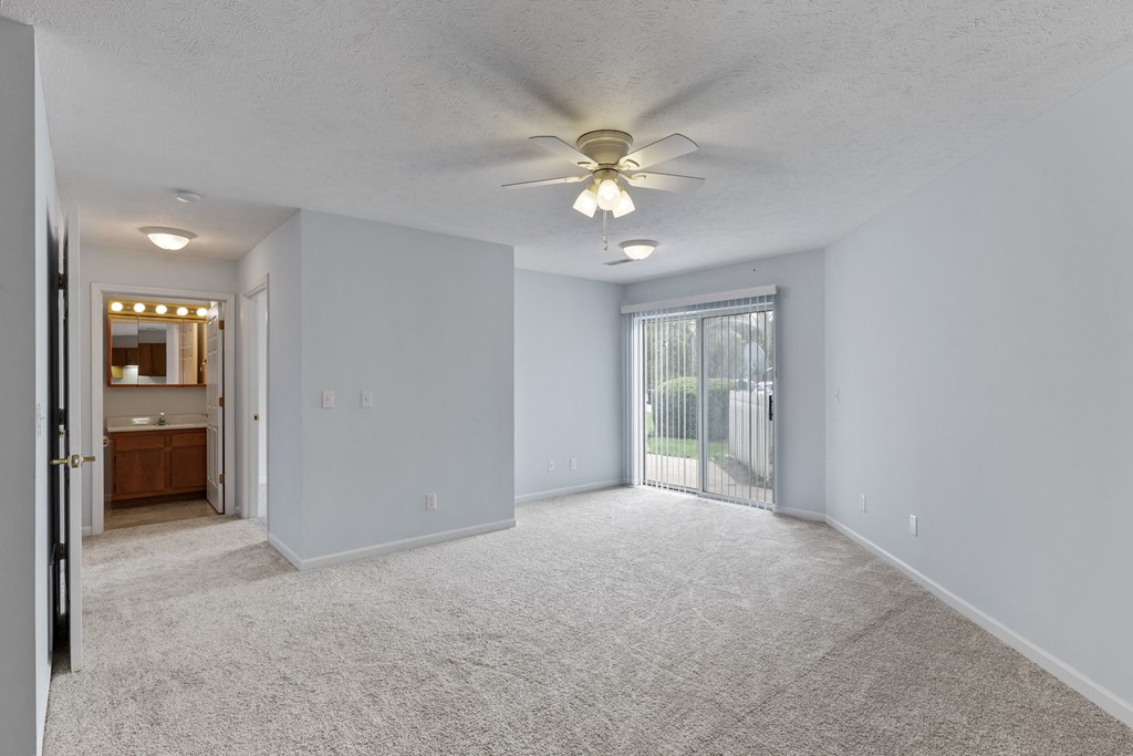 an empty living room with a ceiling fan and a door to a balcony