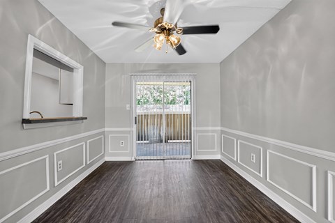 A room with a ceiling fan and a window with a view of trees.
