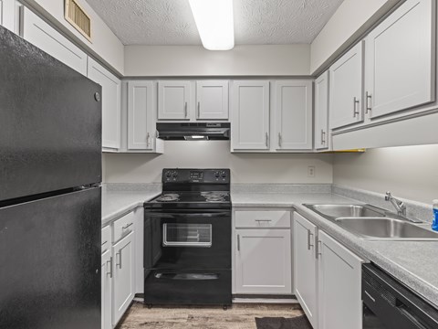 A black refrigerator is on the left in a kitchen with white cabinets.