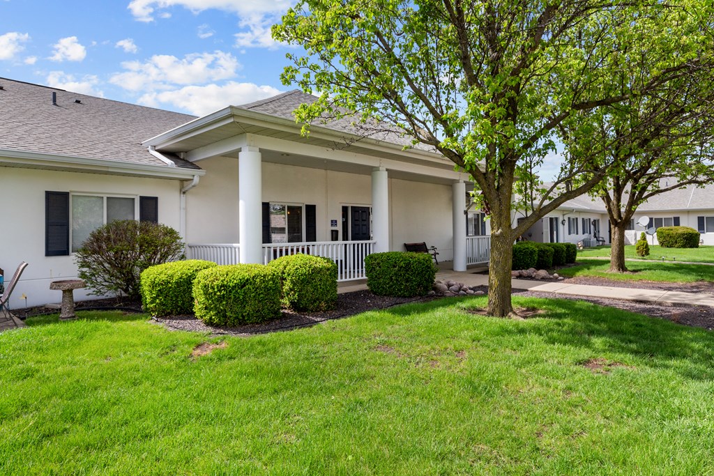a white house with a porch and a tree in the yard