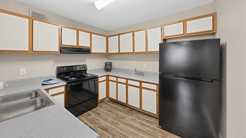 A black refrigerator sits in a kitchen with wooden cabinets.