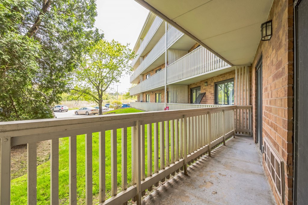 A balcony with a wooden railing and a brick wall on the side.