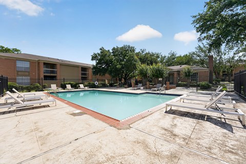 A swimming pool surrounded by a concrete floor and lounge chairs.