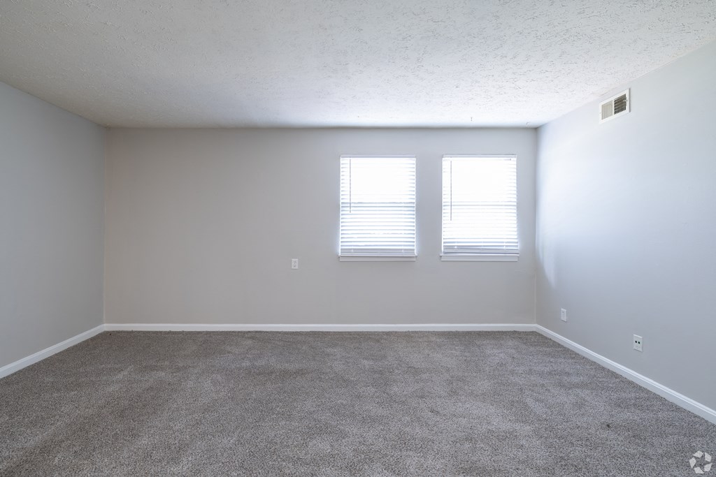 an empty living room with two windows and carpet