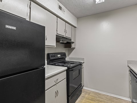 A black refrigerator is in a kitchen with white cabinets.