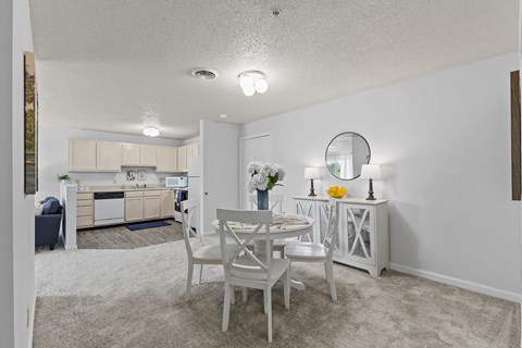 a dining area with a table and chairs and a kitchen in the background