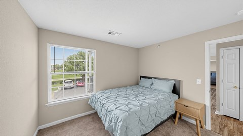 A bedroom with a bed, nightstand, and window overlooking a parking lot.