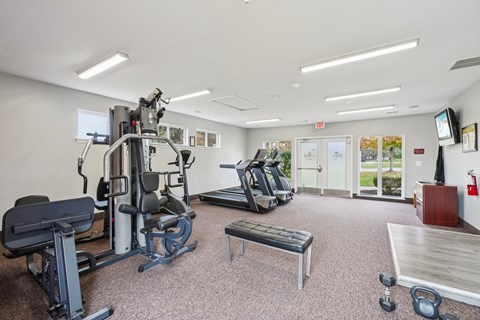 A gym with a variety of equipment including a treadmill, weights, and a bench.