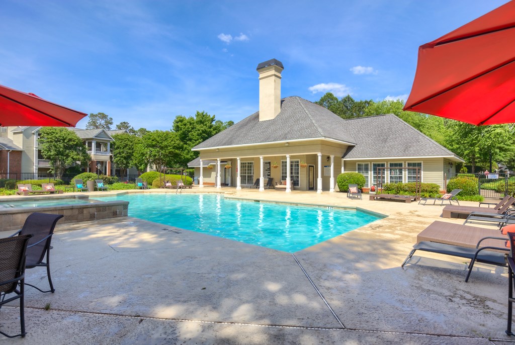 a swimming pool with chairs and umbrellas in front of a house