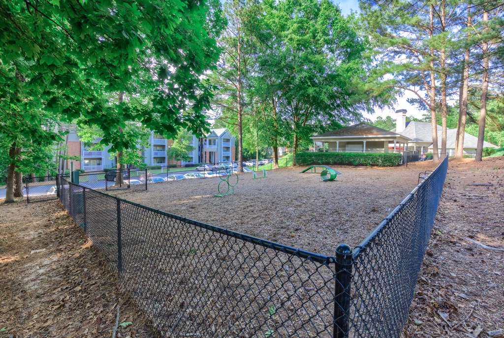 a fenced in dog park with trees and houses in the background