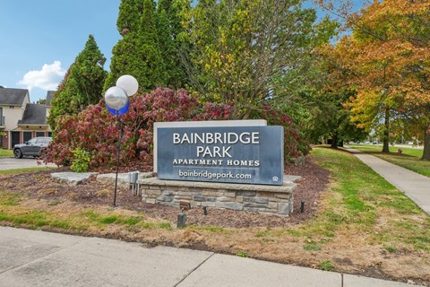 A sign for Bainbridge Park Apartment Homes is in front of a tree.