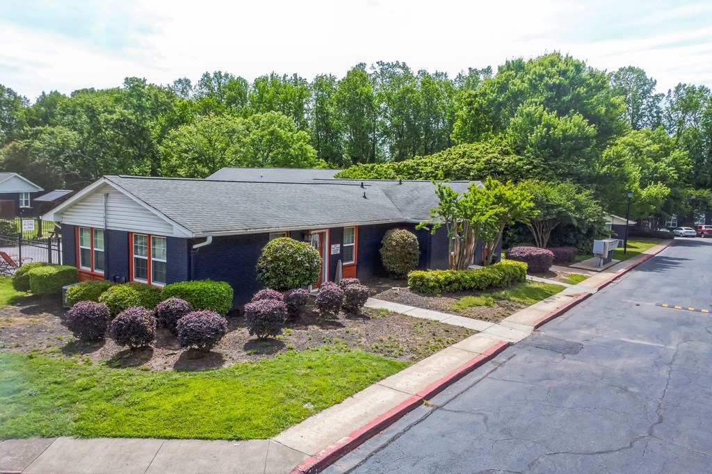 A house with a red trim and a grey roof is surrounded by greenery.