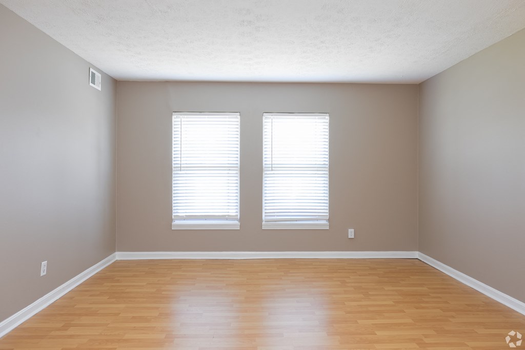 an empty room with wooden floors and two windows