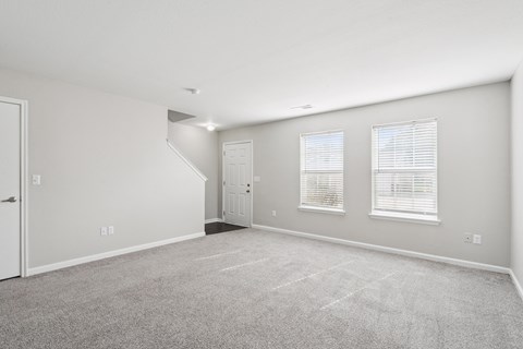 A spacious room with a carpeted floor and a staircase leading to another room.