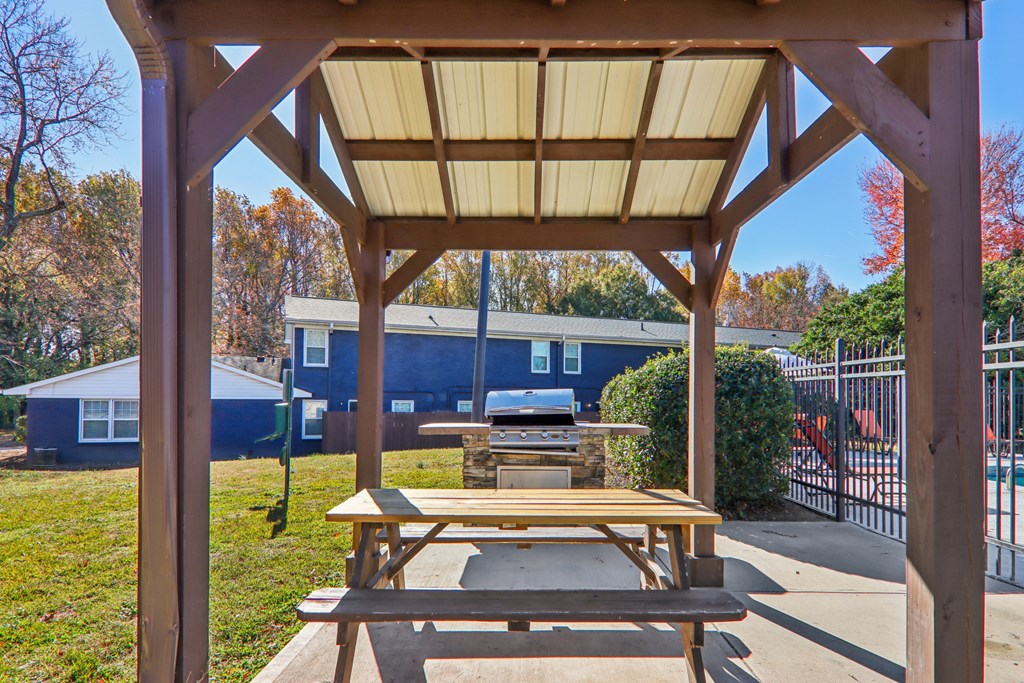 A wooden picnic table is under a shelter in a park.