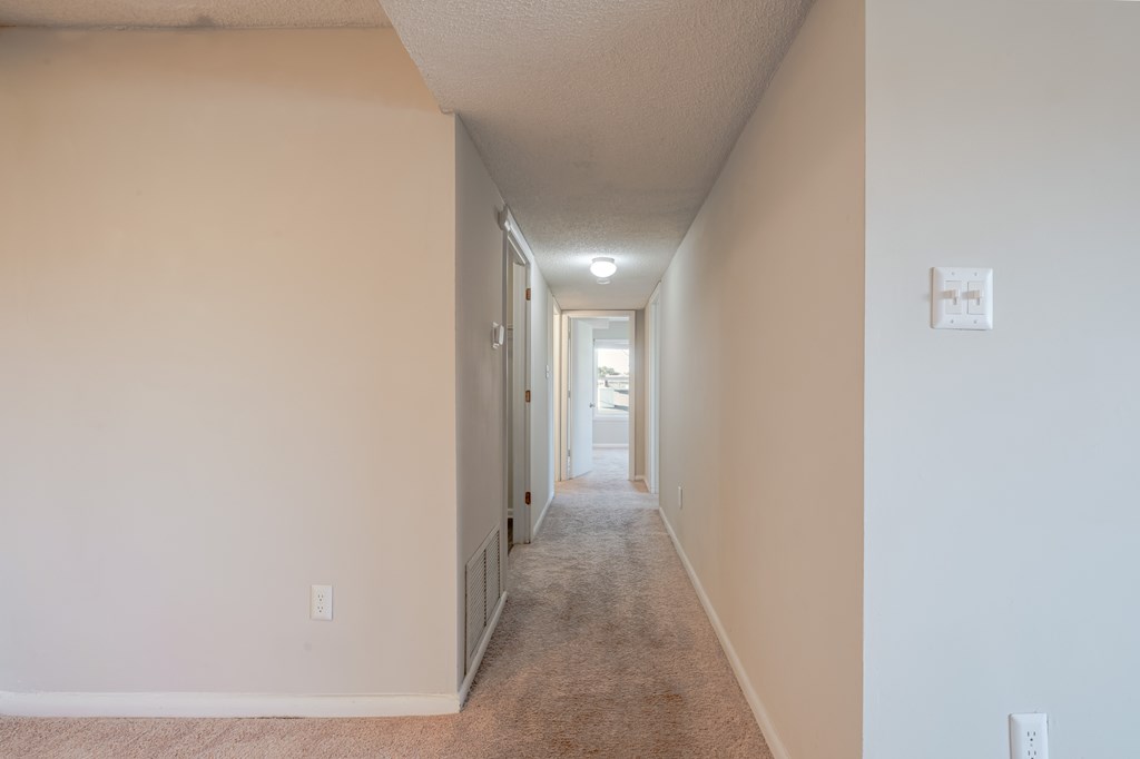 A long hallway with a carpeted floor and white walls.