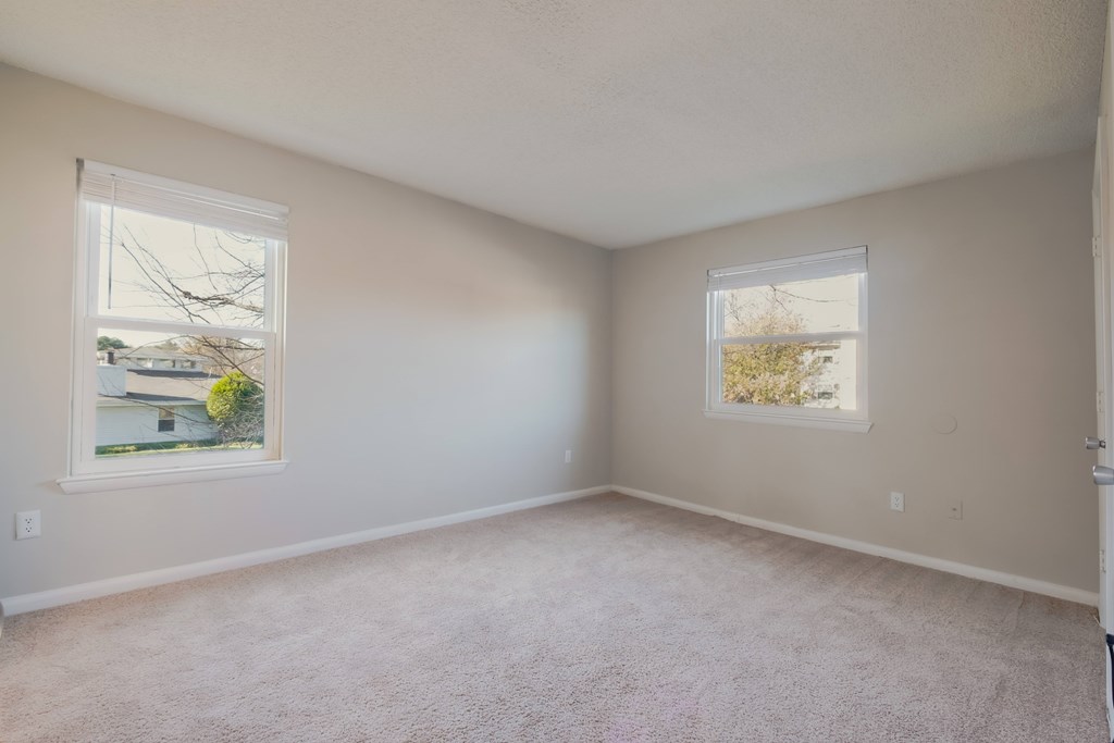 A room with two windows and carpeted floor.