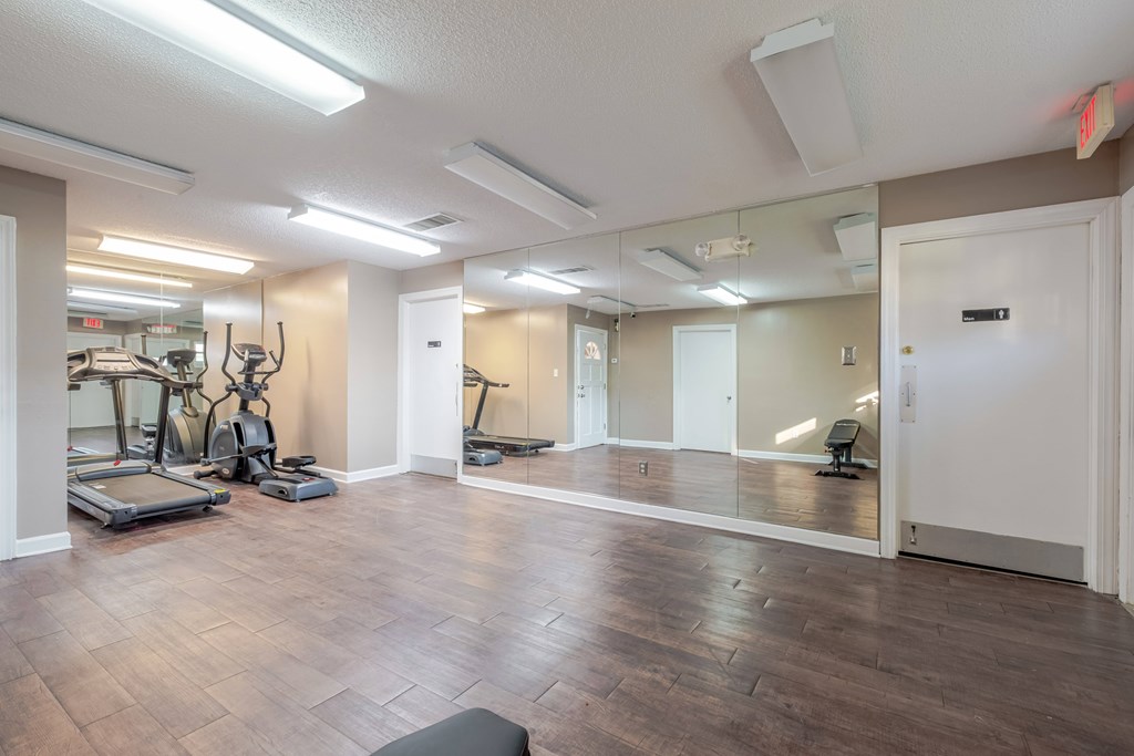 A spacious gym with treadmills, elliptical machines, and mirrors.
