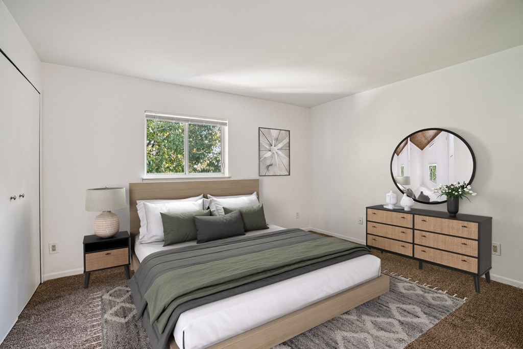 A bedroom with a bed, nightstand, and a round mirror on the wall.