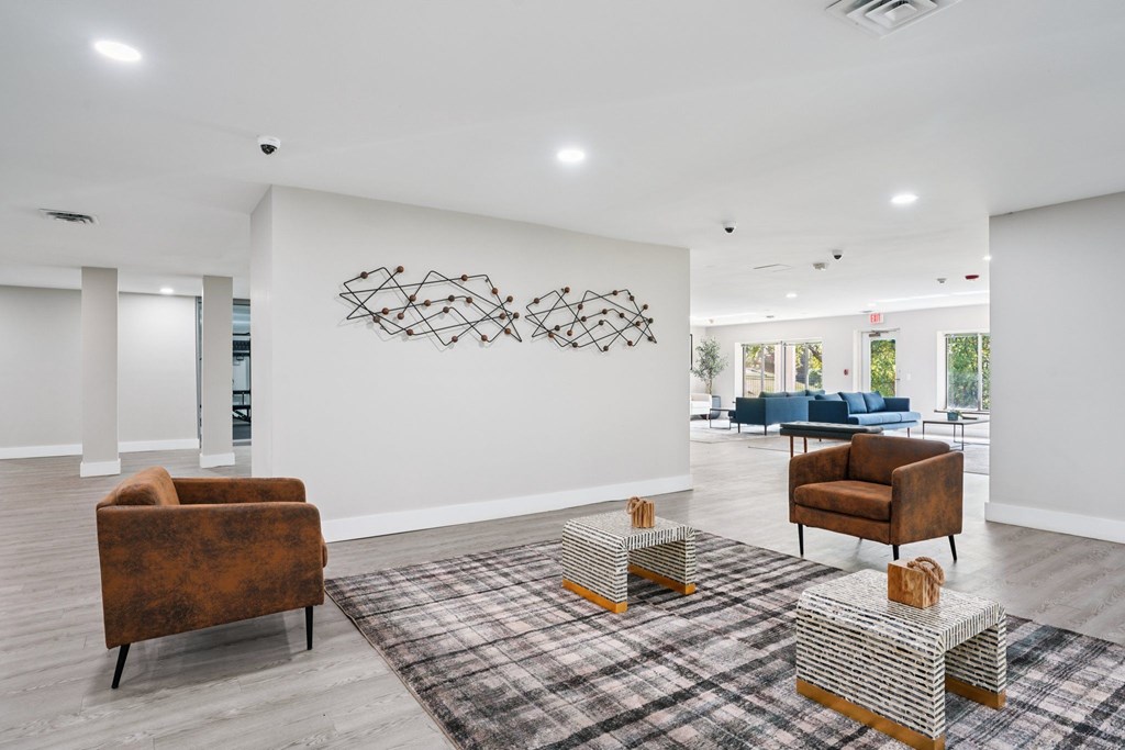 A room with a brown chair, a brown couch, and a wall art.