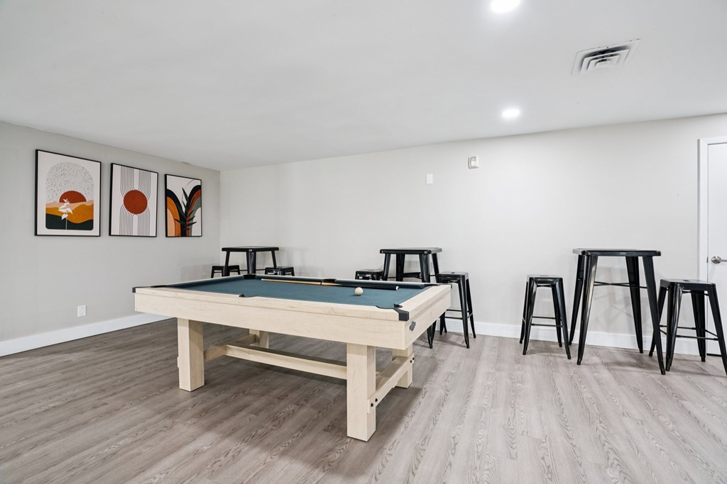 A pool table is in the middle of a room with a bar stool and a painting.