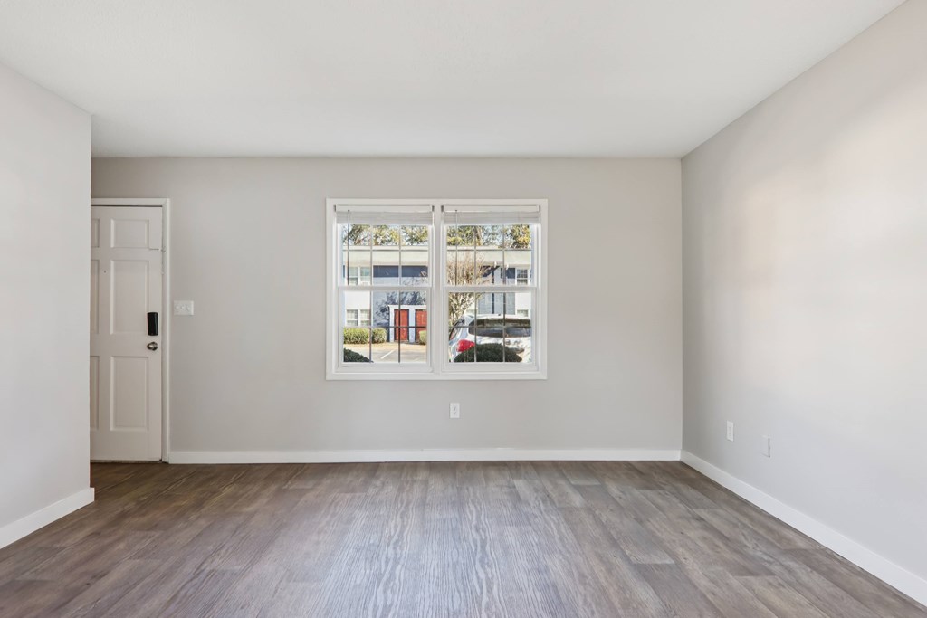 A room with a wooden floor and a window showing a view of a street with cars and buildings.