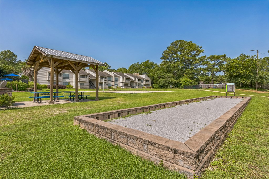 A playground with a sandbox and picnic tables in a grassy area.