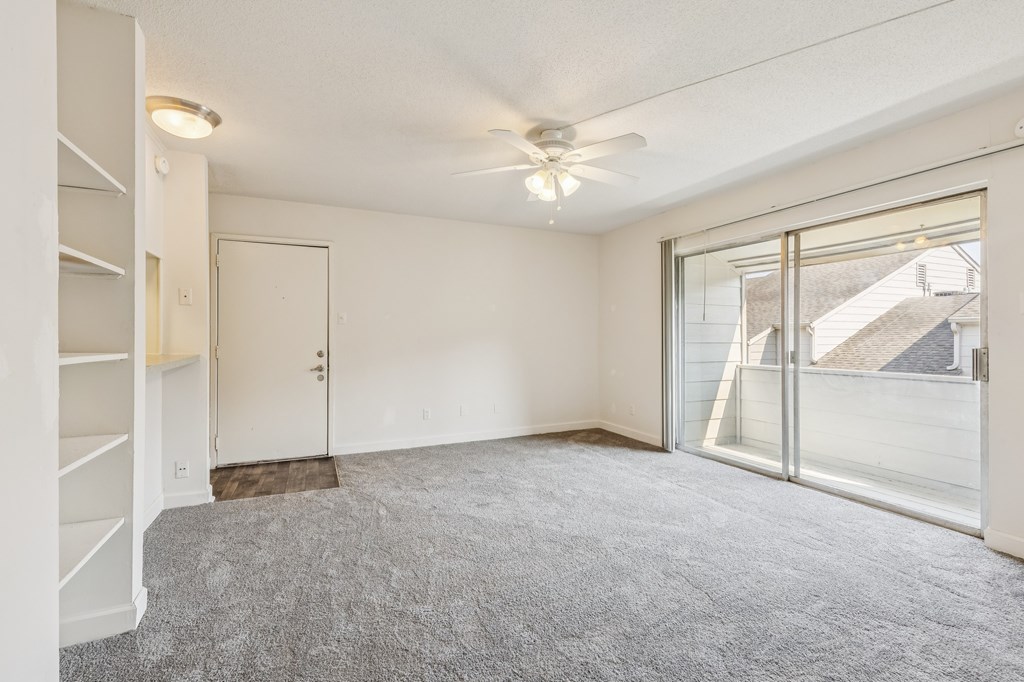 A room with a grey carpet and a ceiling fan.