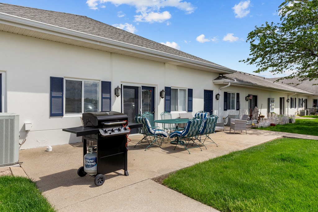 a patio with chairs and a grill in front of a house