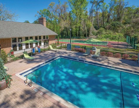 A pool surrounded by a fence with a tennis court in the background.