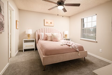 A bedroom with a pink bed and a ceiling fan.