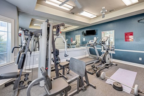 Well-equipped apartment fitness center with exercise machines and wall-mounted television at Cambury Hills Apartments in Omaha, Nebraska