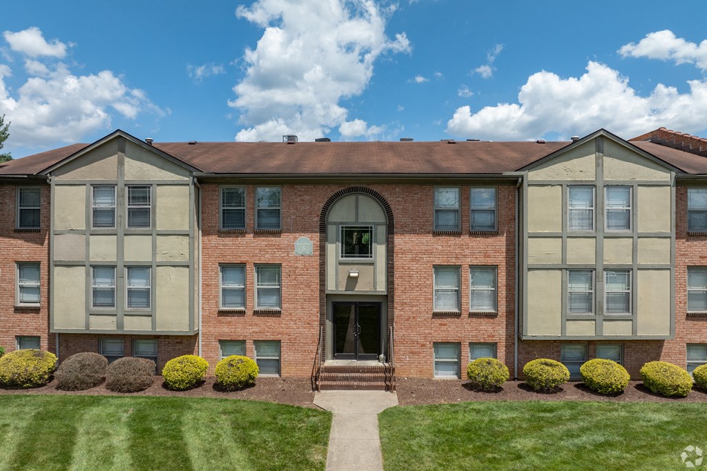 front view of a brick apartment building with green grass and shrubs