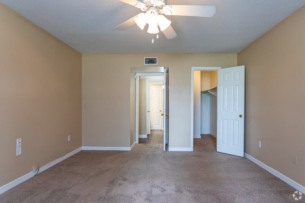 an empty living room with a ceiling fan and a door to a hallway