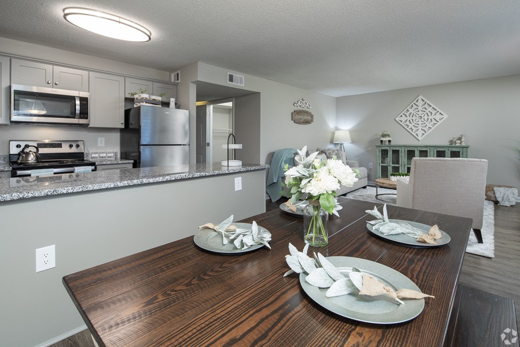 a dining room table with plates and a vase of flowers next to a kitchen