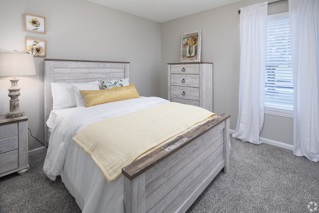 a bedroom with a bed and two dressers and a window