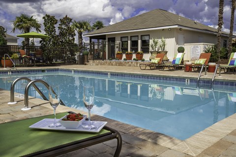 A poolside table with a plate of food and two glasses of wine.