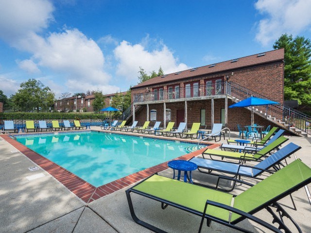 a swimming pool with chaise lounge chairs and umbrellas in front of a brick building