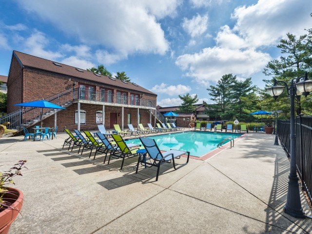 a swimming pool with chaise lounge chairs and umbrellas in front of a brick building